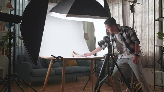 Asian Male Photographer Adjusting Position Of Women'S Shoes And Thinking While Taking Photos Of Them In Home Studio 
