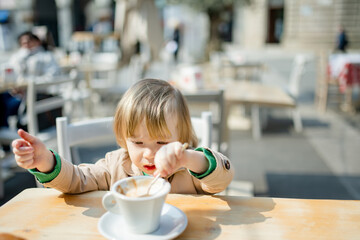 Cute toddler boy having hot chocolate in outdoor cafe. Small child drinking hot beverage on sunny...