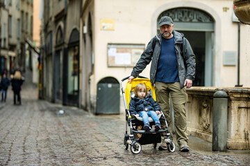 Young father and his toddler son in a stroller walking together down the medieval streets of Bergamo city northeast of Milan. Scenic views of Citta Alta, town's upper district.
