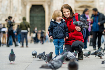 Young mother and her toddler son feeding the pigeons on the Cathedral Square or Piazza del Duomo in the center of Milan, Italy.