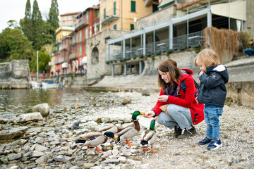 Mother and her toddler son feeding ducks in Varenna, one of the most picturesque towns on the shore of Lake Como. Varenna, Lombardy, Italy.