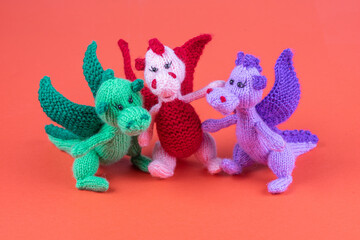 three small knitted dragons on a red background
