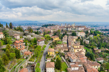 Fototapeta na wymiar Scenic aerial view of Bergamo city. Flying over Citta Alta, town's upper district, known by cobblestone streets and encircled by Venetian walls. Bergamo, Lombardy, Italy.
