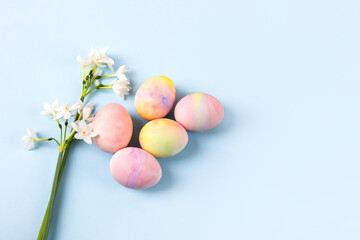 Fototapeta na wymiar Spring white flowers daffodils and pink Easter eggs on a blue background with space for text. Happy Easter concept. Greeting card, copy space