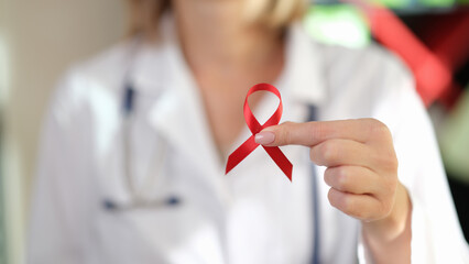 Female doctor holds red ribbon in her hand as symbol of International AIDS Day.