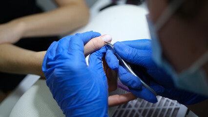 Manicurist in latex gloves cuts cuticle of client's finger.