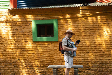 Caucasian young man, father carrying little newborn baby in carrier,family traveling, going sightseeing in center of La Boca quarter, Buenos Aires, Argentine, looking at bright colourful buildings.