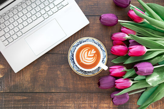 top view of desktop, tulips, laptop and coffee on wooden table.