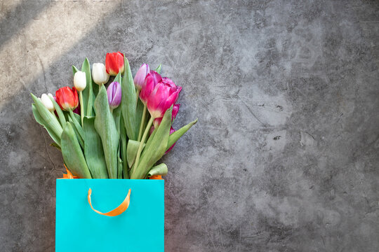 Fresh tulips flowers in blue paper bag on grey background. Top view with copy space.