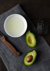 Avocado oil and Halves of fresh organic Avocado on the wood background, top view, flat lay