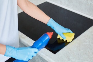 Female hand cleaning black glass induction stove. Woman use sponge, making surface clean on...