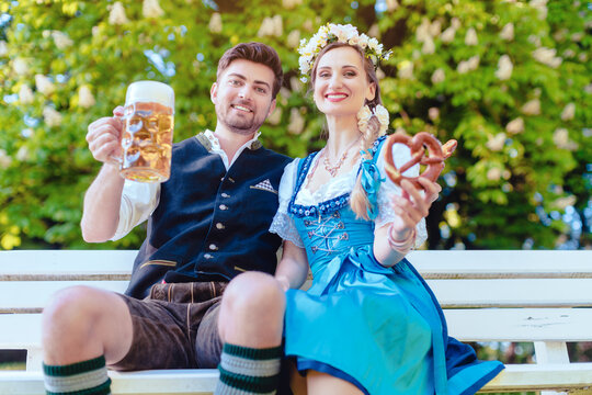 Couple in Bavaria sitting on bench toasting with beer hugging each other