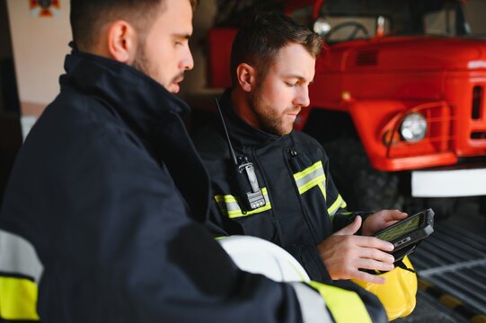 Portrait of two firefighters in fire fighting operation, fireman in protective clothing and helmet using tablet computer in action fighting - Powered by Adobe