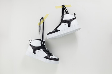Pair of modern trendy sneakers hang on laces on color wall. White and black unisex sport footwear...