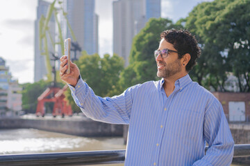 Middle-aged Latin man making a video call on a pedestrian bridge while getting to know the city.