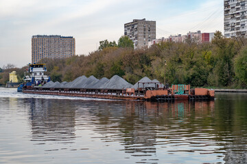 Obraz premium Barge loaded with sand or grey gravel floats on wide river