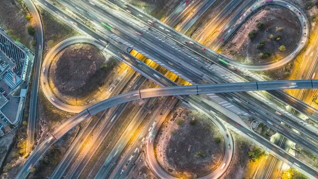 Beautiful top view time-lapse (day to night) of car traffic at multiple lane highway. Aerial view zoom out of highway road intersection and city traffic at night. Urban cityscape concept, Spain