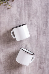 Two white empty metal mugs on a gray background in a vertical view. Top view