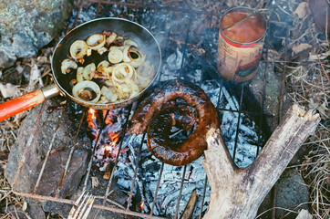 Fried onions venison meat and a can of beans over a grill and fire on the forest floor