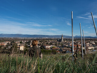Woman sitting in the middle of vineyard and enjoying the view of Cornas village and church with...