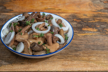 Salted Suillus mushrooms served with onion and fresh thyme in ceramic bowl over wooden background.