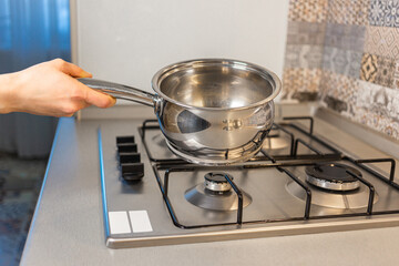 The girl is placing a pot on the stove, preparing to cook a dish that requires boiling or simmering.