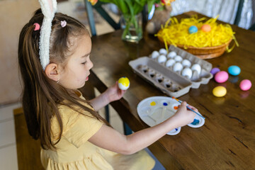Little girl coloring easter eggs in yellow 