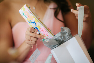 bridesmaid in pink dress taking colorful purse out of a paper gift bag 