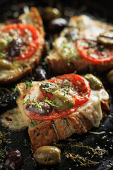Grilled cheese toast with tomatoes and olives seasoned with thyme on a black background, close up view