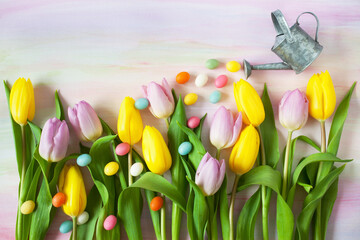 Yellow and purple tulips, watering can and candy eggs on colorful watercolor paper background. Easter spring card, copy space. - Powered by Adobe