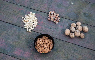Top view of a rustic wooden table filled with an assortment of nuts like hazelnuts, almonds, pistachios, and walnuts. The almonds are in a black bowl. 