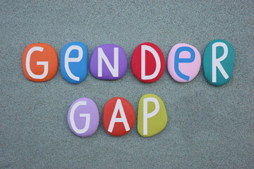 Gender gap, social issue text composed with multi colored stone letters over green sand
