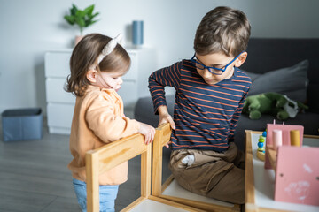 Two children brother and sister playing at home and trying to adjust the chairs, early child development, playing and learning, modern family concept