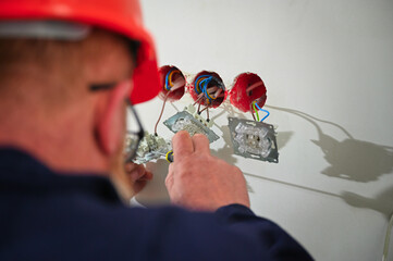 Professional electrician technician installing a wall socket in a new house. Electrical repairs at...