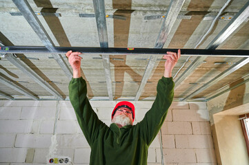 Construction worker in protective helmet holding spirit level at construction site preparing metal...