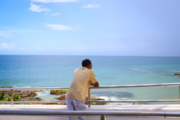 Fototapeta premium Man watching the beach, sea, the rocks, the clouds and the blue sky