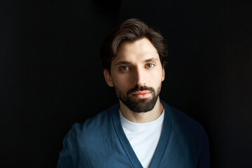 Male appearance. Portrait of smart clever handsome gorgeous man entrepreneur or real estate agent of 30 in blue cardigan sweater posing against black studio background, looking at camera