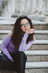 Fototapeta premium Beautiful young woman with brunette curly hair, portrait in eye glasses enjoying the sun in the city.