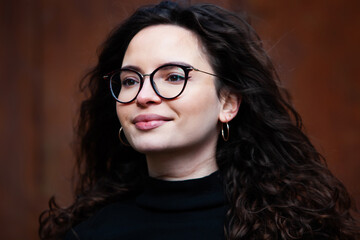 Fototapeta na wymiar Beautiful young woman with brunette curly hair, portrait in eye glasses enjoying the sun in the city.