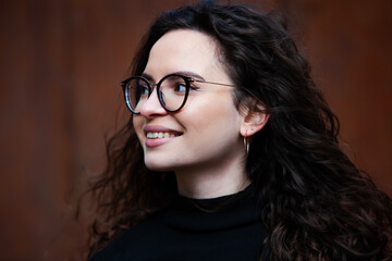Fototapeta na wymiar Beautiful young woman with brunette curly hair, portrait in eye glasses enjoying the sun in the city.