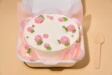 Small Korean style trendy bento cake decorated with pink cream cheese flowers in a white gift box on the beige background. Cake as a gift for a beloved one. Spring tender cake for a woman. Top view