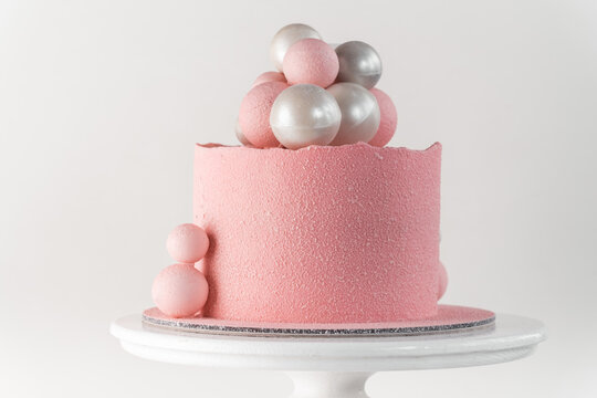 Birthday cake with pink velvet sprayed coating decorated with silver and pink chocolate spheres on the white background
