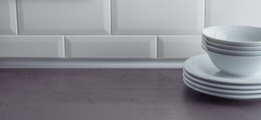White plates on grey textured countertop on a white tile wall background. Table setting concept.