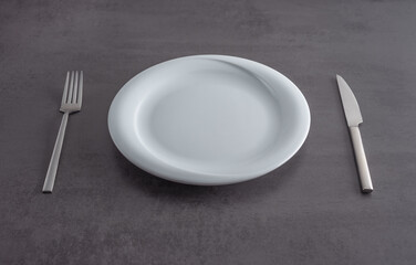 White plate, fork and knife on a grey textured kitchen countertop. Table setting concept.