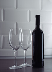 Wine bottle and two wine glasses on grey textured countertop on a white tile wall background. Table setting concept.