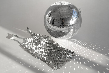 Mirror ball and chain mail dress on a white floor with sunbeams. Mirror items and sunlight reflections. 