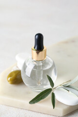 Board with bottle of olive essential oil on light background, closeup