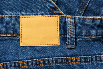 Fashion background with empty copy space for graphic design. Blank leather label tag. Blue jeans denim texture with thread sew lines. Brown clothing tag.