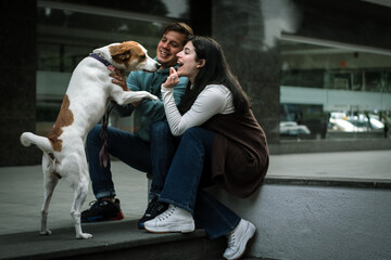 Happy couple giving treats to their dog in the city. Happy dog with his family in the city. Happy family with their dog in the city