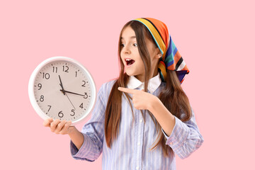 Little girl pointing at wall clock on pink background